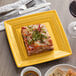 A Tuxton Concentrix saffron square china plate with a slice of lasagna on a table with silverware and a glass of wine.