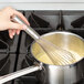 A hand using a Vollrath stainless steel whisk to stir liquid in a pot.