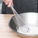 A person using a Vollrath stainless steel piano whisk to stir flour in a bowl.