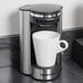 A Conair Cuisinart single cup coffee maker with a white cup on a black coaster.