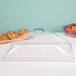 A Cambro clear plastic dome display cover with 2 end cuts on a tray of doughnuts.