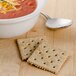 A bowl of red soup with Lance Whole Grain Saltine crackers and cheese on a table.