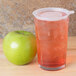 A Cambro plastic tumbler filled with a pink drink on a white background next to a green apple.