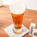 A Libbey pilsner glass of beer on a table with a napkin and salt and pepper shakers.