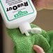 A hand using a green towel to clean a white bottle of Unger RubOut glass cleaner.