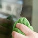 A hand using a green cloth to clean a window with Unger RubOut Glass Cleaner.