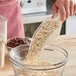 A hand using a Choice clear plastic utility scoop to pour oats into a bowl.