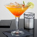 A Libbey martini glass filled with an orange cocktail and garnished with lime wedges.