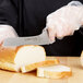 A person in gloves using a Dexter-Russell Sani-Safe Scalloped Offset Bread and Sandwich Knife to cut bread on a counter.