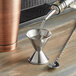 An American Metalcraft stainless steel jigger with .75 oz. and 1.5 oz. measurements on a table.