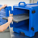 A hand placing a grey plastic shelf on a blue Cambro container.
