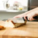 A person using a Victorinox bread knife to cut bread on a cutting board.
