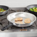 Two Vollrath Wear-Ever aluminum fry pans with meat and vegetables cooking on a stove.