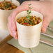 A hand holding a Tablecraft small wooden serving cup with food.