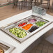 A Vollrath stainless steel oval pan filled with a variety of vegetables on a buffet counter.