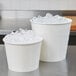 Two Lavex white paper ice buckets filled with ice on a table.