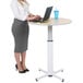 A woman standing at a Luxor round pneumatic adjustable height table using a laptop.