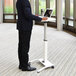A man in a suit standing at a white Luxor pneumatic adjustable height lectern using a laptop.