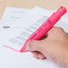 A hand holding a Universal fluorescent pink highlighter pen over a paper.
