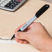 A hand using a Universal black fine point permanent marker to write on a piece of paper.
