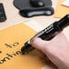 A person using an Avery Marks-A-Lot black desk style permanent marker to write on a piece of paper.