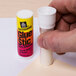 A hand holding a white tube of Avery Glue Stic.