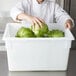 A chef putting lettuce in a white Rubbermaid food storage container.