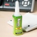 A green Krazy Glue bottle with a white cap sitting on a table next to a white object.