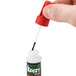 A hand holding a Krazy Glue bottle with a red cap and black liquid inside.
