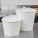 Two white Lavex paper ice buckets on a table with ice in them.