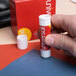 A hand holding a red and white Universal clear glue stick.