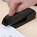 A person using a Universal black executive desktop stapler to staple a document.