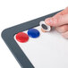 A hand holding a magnet on a Universal white magnetic dry erase board.