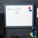 A white Universal magnetic melamine dry erase board with a charcoal frame and magnets on a grey surface.