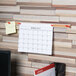 A brown Universal cork bulletin bar with a calendar hanging on a wall.