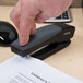 A person's hand using a black Universal stand up stapler to staple a piece of paper.