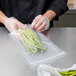 A person in a black apron holding an ARY VacMaster chamber vacuum packaging bag of green beans.