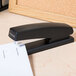 A black Universal full strip stapler on a desk with paper.