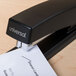 A Universal black full strip desktop stapler with a piece of paper in it.