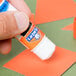 A hand using an orange and white Elmer's Clear School Glue Stick to make a paper craft.