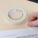 A hand using Universal masking tape to cover a roll of paper.