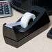 A black and white Universal tape dispenser on a desk with a roll of clear tape in a black box.