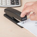 A person using a Universal black half strip stapler to staple paper on a table.