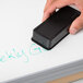 A hand using a Universal synthetic wool felt dry erase eraser to erase a black marker drawing on a whiteboard.