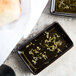 A rectangular black Tuxton China sauce dish with green liquid and herbs on a plate.