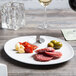 A TuxTrendz bright white china appetizer plate on a table with a glass of wine.