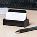 A black Universal business card holder on a white desk.