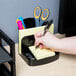 A black Universal plastic organizer with sections holding a pen, note pad, and scissors.