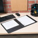 A black Avery Economy View Binder on a desk with papers and a computer.