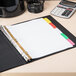 A binder with Avery Big Tab Write & Erase dividers on a desk with a white paper and calculator.